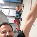 Jay and his child striking a pose while engaging in wall climbing, displaying their adventurous spirit and shared excitement during the activity.