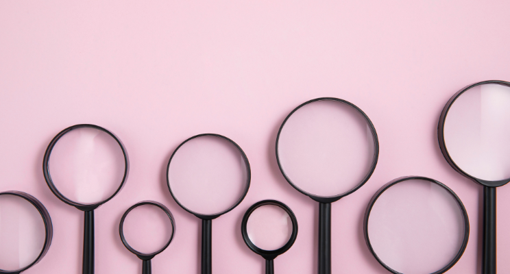 Various lengths of black magnifying glasses arranged on a pink background, illustrating a visual representation of diversity or options for magnification.