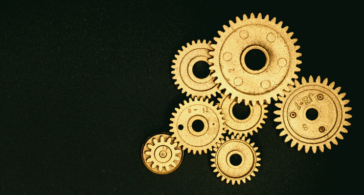 Golden gears of various sizes positioned against a black background, representing precision, interconnectivity, and the mechanics of a well-functioning system.