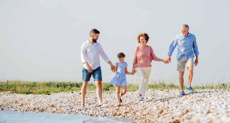 A multigenerational family, spanning different age groups, walking hand in hand on a pebble beach, symbolizing unity, connection, and shared moments of joy.