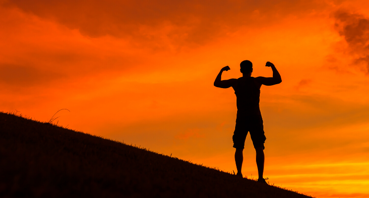 The silhouette of a man standing on a hill, flexing his biceps, showcasing strength, determination, and a sense of achievement.