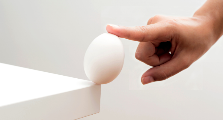 A finger delicately balancing an egg on the edge of a table, showcasing a feat of stability and precision.